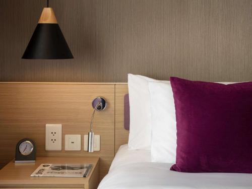 a bed with a purple pillow and a table with a clock at Mercure Hai Phong in Hai Phong