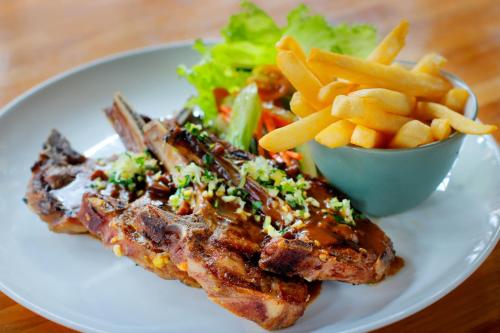 a white plate with meat and french fries and a salad at Sagara Candidasa by AHM in Candidasa