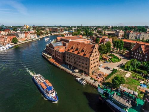 a boat is docked on a river in a city at Jess Krolewski Gdansk Old Town in Gdańsk
