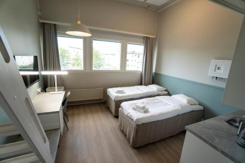 a room with two beds and a desk and windows at Innotelli Apartments in Helsinki