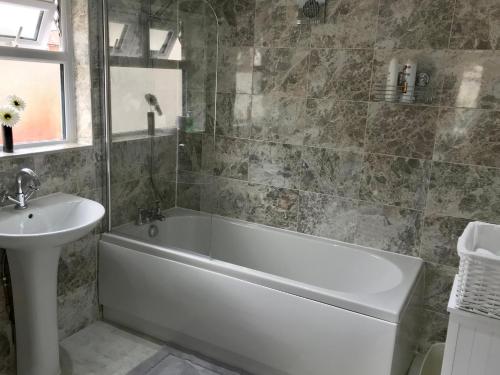 a bathroom with a white bath tub and a sink at The Woodfarm Lodge - 3 Bedroom House with free Parking in Oxford