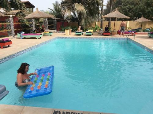 a woman in a swimming pool with a giant board in the water at Calabash Apartment-Hotel in Kotu