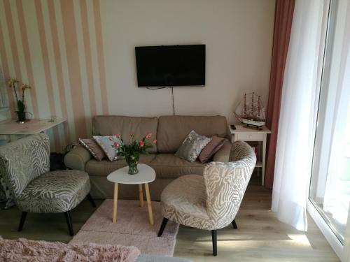ein Wohnzimmer mit einem Sofa, Stühlen und einem TV in der Unterkunft Baltic Park Kryształowy apartament in Pogorzelica