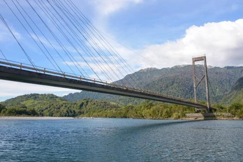 a bridge over a river with mountains in the background at Alto Melimoyu Hotel & Patagonia in La Junta