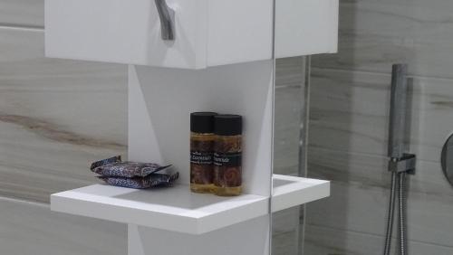 a white shelf with two bottles of spices next to a shower at Bistrica Hotel in Sarandë