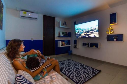 a woman and a child sitting on a couch watching tv at Casa del Puerto Hostel & Suites in Cartagena de Indias