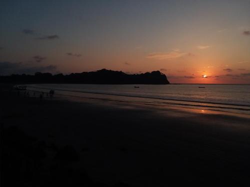 a sunset on a beach with a mountain in the distance at Hostal Camping Sin Fronteras Mompiche in Mompiche
