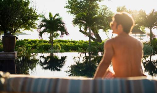 a man sitting in front of a swimming pool at Raffles Seychelles in Baie Sainte Anne