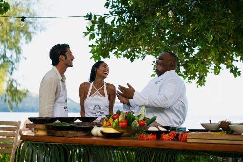 a group of three people standing around a table with food at Raffles Seychelles in Baie Sainte Anne