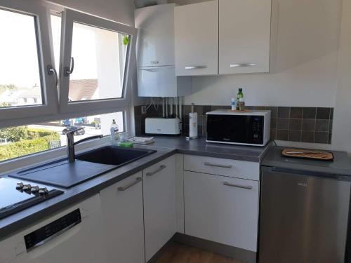 a kitchen with white cabinets and a sink and a microwave at Le bélouga in Sangatte