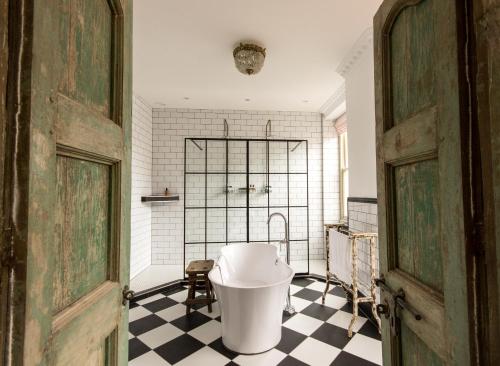 a bathroom with a white tub and a checkered floor at The Crooked Swan in Crewkerne