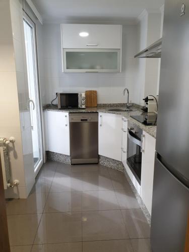 kuchnia z białymi szafkami i urządzeniem ze stali nierdzewnej w obiekcie APARTAMENTOS PORTA NOVA w mieście Lugo