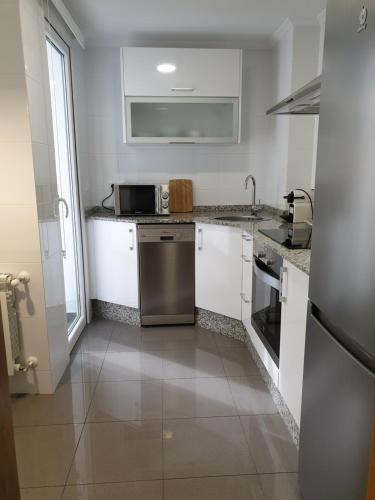 una cocina con armarios blancos y un aparato de acero inoxidable en APARTAMENTOS PORTA NOVA, en Lugo
