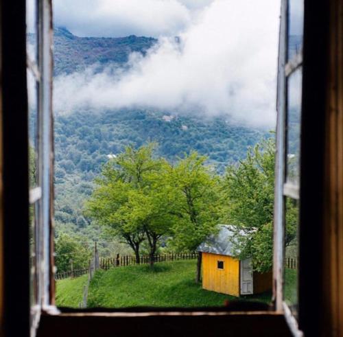a window view of a yellow house and a mountain at Guesthouse Dritan Tethorja in Theth