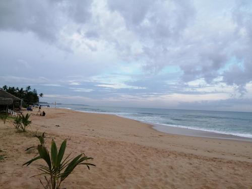 a beach with people sitting on the sand and the ocean at Beach Lagoon Guesthouse in Tangalle