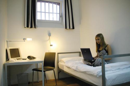 a woman sitting on a bed with a laptop at ALCATRAZ Hotel am Japanischen Garten in Kaiserslautern