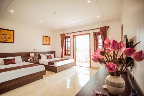a bedroom with two beds and a vase with pink flowers at Salina Hotel Ninh Binh in Ninh Binh