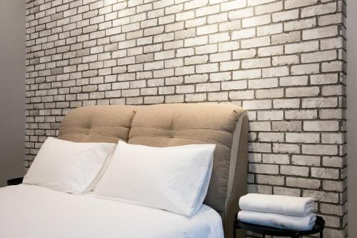 a bed with white pillows in front of a brick wall at Canning 33 in Ipoh