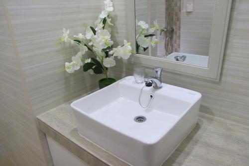 - un lavabo blanc dans la salle de bains pourvue d'un vase de fleurs dans l'établissement RNR Suites, à Legazpi