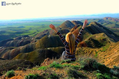 a woman sitting on top of a mountain with her arms in the air at My home udabno in Udabno
