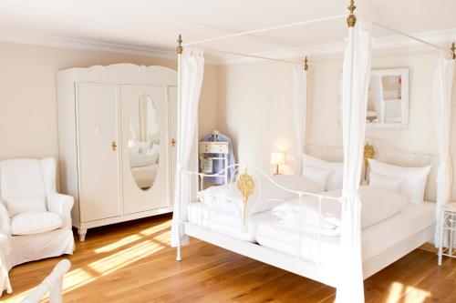 a white bedroom with a white canopy bed and a chair at Landhaus Marinella Hotel Garni in Bad Wiessee