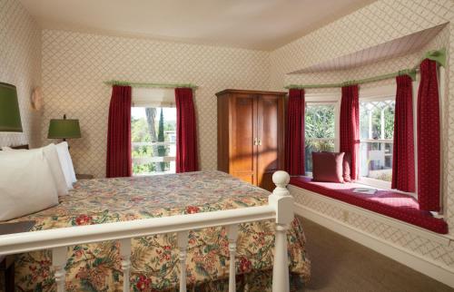 a bedroom with a bed and two windows with red curtains at Cheshire Cat Inn & Cottages in Santa Barbara