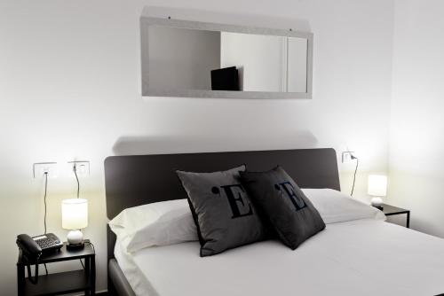 a white bed with black pillows and a mirror at L'Essenza Hotel in Olbia