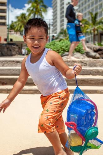 a young boy walking on the beach with a bag at VIVE Hotel Waikiki in Honolulu