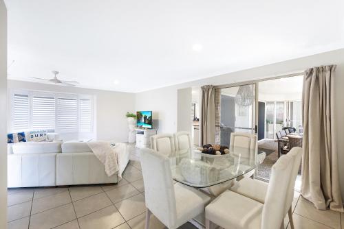 a white living room with a glass table and white chairs at Sweetbrush Place in Mooloolaba