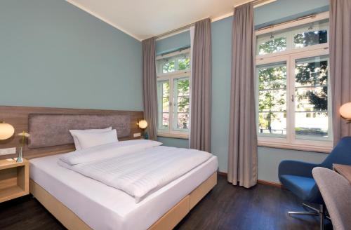 a bedroom with a bed and a chair and windows at Hotel Savigny Frankfurt City in Frankfurt/Main