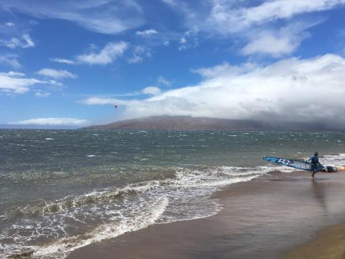 a man walking on the beach with a surfboard at Perfect for families and couples - Maui Sunset A-203 in Kihei