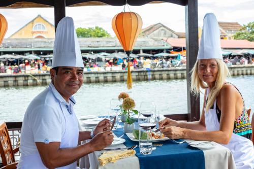 a man and woman sitting at a table with chefs hats on their heads at Little Riverside Hoi An . A Luxury Hotel & Spa in Hoi An