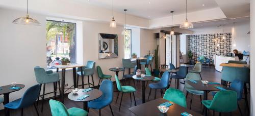 ニースにあるホテル ルレ アクロポリスの青と緑の椅子とテーブルが備わるレストラン