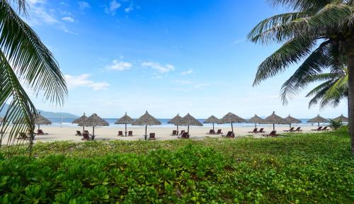 a beach with many straw umbrellas and the ocean at Furama Villas Danang in Da Nang