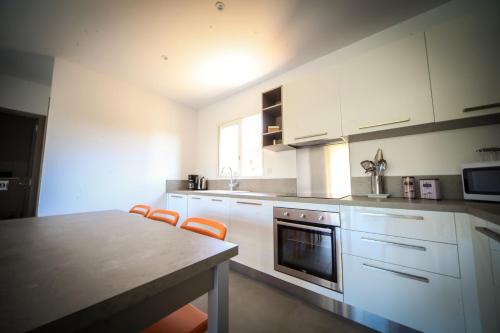 a kitchen with white cabinets and a table with orange chairs at SARL Valinco locations appartement 2 chambres in Olmeto