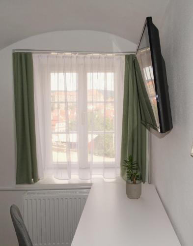a desk with a television and a window with green curtains at Hotel Garni Villa Areka in Český Krumlov
