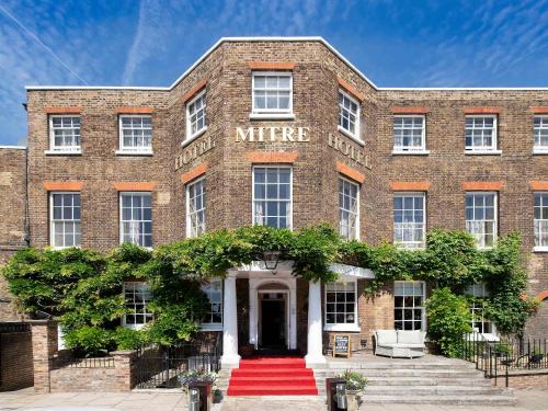 um antigo edifício de tijolos com uma entrada de tapete vermelho em The Mitre, Hampton Court em Kingston upon Thames