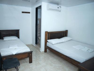 two beds in a room with a chair at Aparta Hotel El Cacique Upar in Valledupar