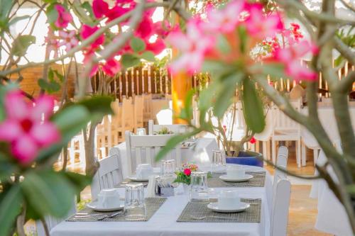 una mesa con sillas blancas y flores rosas. en Pousada Windjeri en Jericoacoara