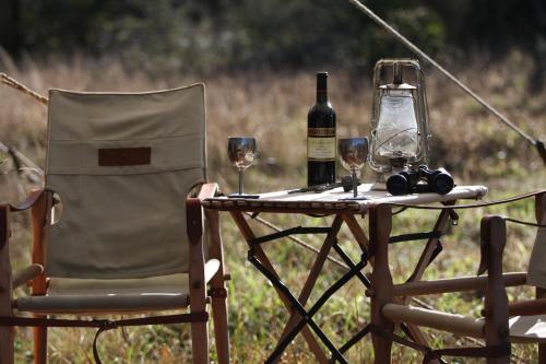 a table with two glasses of wine and a chair at Quatermain's 1920's Safari Camp – Amakhala Game Reserve in Amakhala Game Reserve