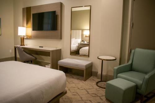 a hotel room with a bed and a chair and a mirror at Centennial Plaza Resort Gulfport in Gulfport