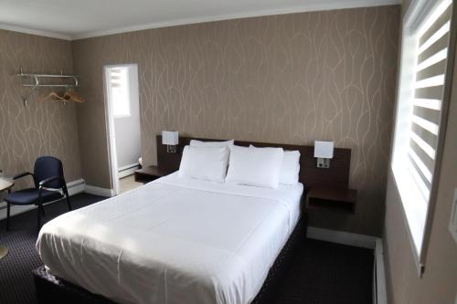 Habitación de hotel con cama blanca y silla en Walkerton Inn Motel, en Walkerton