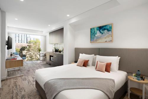 a bedroom with a large white bed and a kitchen at Quest North Sydney in Sydney