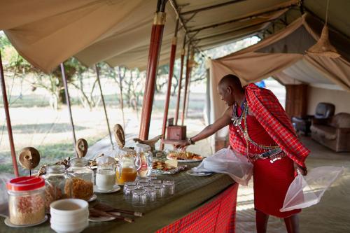 a woman preparing food at a table in a tent at Mara Siria Tented Camp & Cottages in Aitong