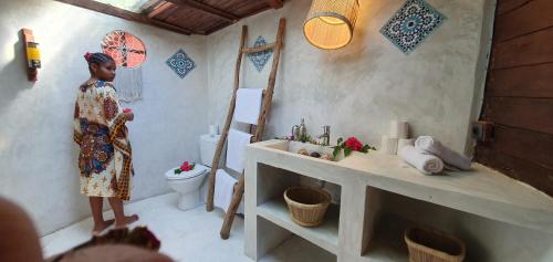 a woman standing in a bathroom with a toilet at Hotel ECOLODGE LE RAVORAHA in Sainte Marie