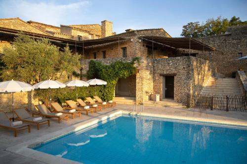 a pool with chairs and umbrellas next to a building at Mas des Herbes Blanches Hôtel & Spa – Relais & Châteaux in Joucas