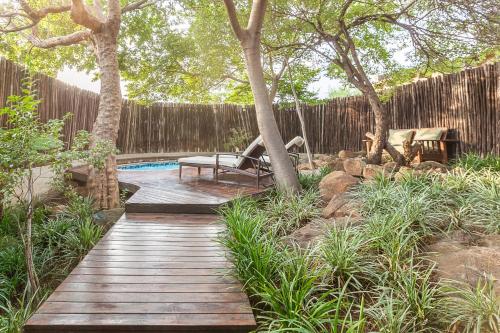 a wooden pathway leading to a pool with a bench and trees at Riverstone Lodge in Muldersdrift
