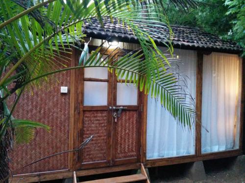 a small cabin with a door and a palm tree at Village Susegat Beach Resort in Morjim