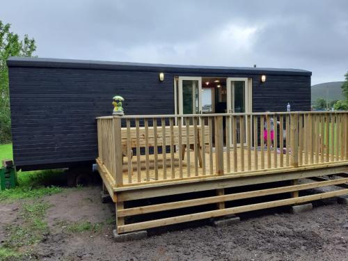 een zwart tiny house met een houten terras bij Annascaul Train Carriage suit couple and 2 children in Anascaul