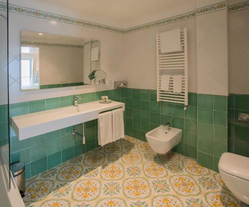 a green and white bathroom with a sink and a toilet at Lloyd's Baia Hotel in Vietri sul Mare